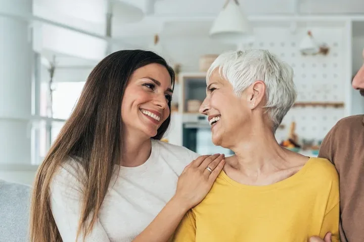An adult daughter and son either side of their mother, talking and smiling at home
