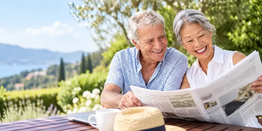 A retired couple reading the newspaper together outdoors on a sunny day