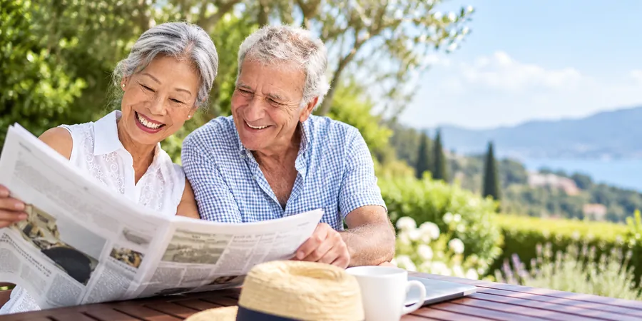 A retired couple reading the newspaper together outdoors on a sunny day