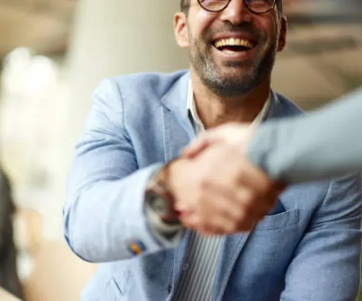Two people shaking hands across a table, both smiling