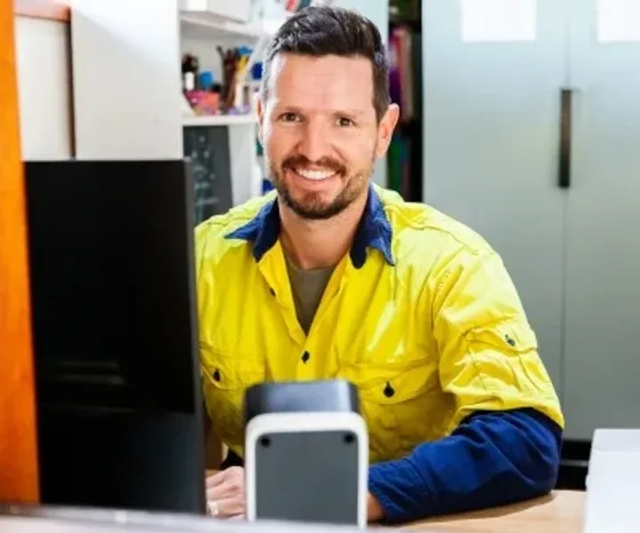 A tradesperson in a hi-vis shirt at a desk in a workshop office