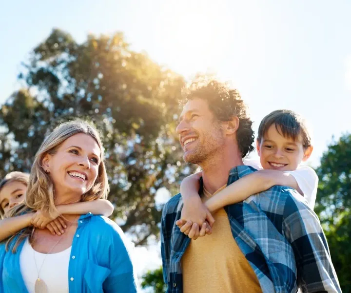 Parents outdoors in the sun carrying their two children on their backs