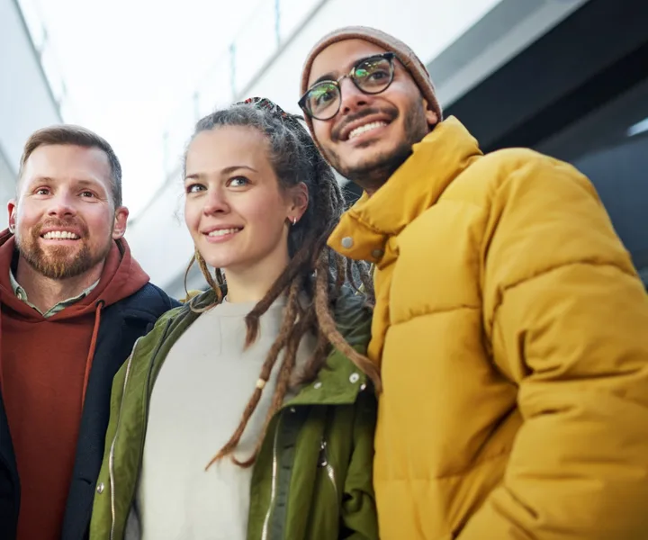 Three smiling young adults in winter jackets standing together outdoors