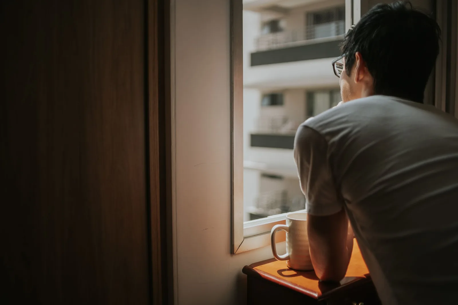 Man holding a mug and looking out of a window